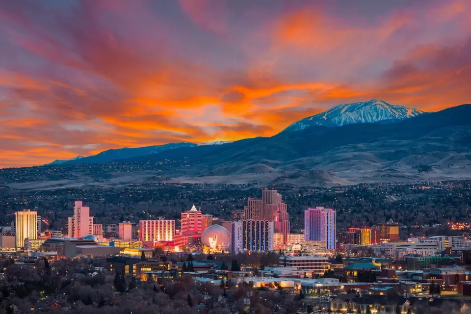 Skyline of Reno, Nevada against snowy mountains and bright red sunset sky.